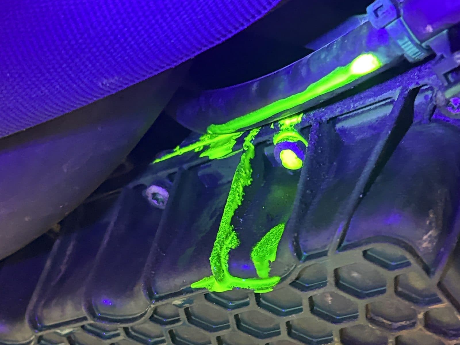 UV dye glowing bright green under blacklight at Zoom Automotive in Lynchburg, Virginia, showing where fluid is seeping out of a joint and running down the housing below it